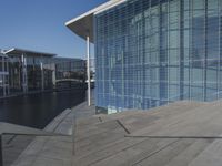 a large blue glass building next to water and buildings with blue windows and grey concrete flooring