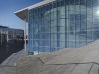 a large blue glass building next to water and buildings with blue windows and grey concrete flooring