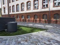 a garbagecan outside a brick building in a courtyard area and sidewalks around it