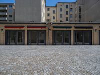 the sidewalk is paved with stones and has a bench in front of it, with no people inside