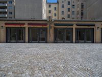 the sidewalk is paved with stones and has a bench in front of it, with no people inside