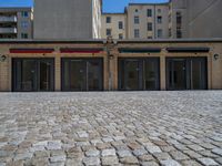 the sidewalk is paved with stones and has a bench in front of it, with no people inside