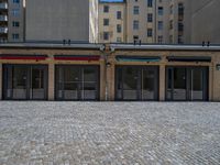 the sidewalk is paved with stones and has a bench in front of it, with no people inside