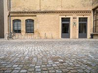 a bicycle parked in front of a tall brick building in an empty courtyard area,