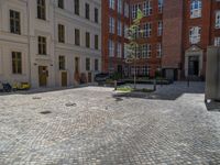 a green shrub near a gray building and a brick walkway with a bicycle rack in it