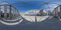 a fish - eye lens captures a curved walkway, a structure with arches and pillars on both sides