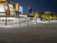 an empty courtyard at night with the city skyline in the background while the street is dark