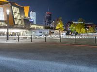 an empty courtyard at night with the city skyline in the background while the street is dark