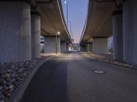 a paved area in between two highway bridges with lights on them and rocks underneath it