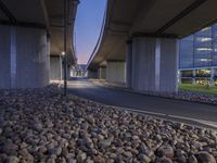 a paved area in between two highway bridges with lights on them and rocks underneath it