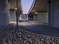 a paved area in between two highway bridges with lights on them and rocks underneath it