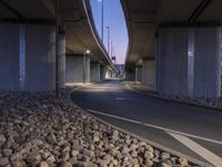 a paved area in between two highway bridges with lights on them and rocks underneath it