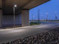 a paved area in between two highway bridges with lights on them and rocks underneath it