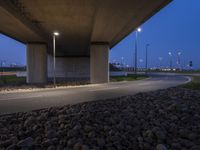 a paved area in between two highway bridges with lights on them and rocks underneath it