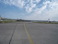 an airport runway with blue skies and some yellow lines on it and clouds in the background