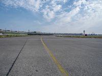 an airport runway with blue skies and some yellow lines on it and clouds in the background