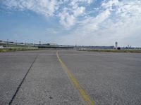 an airport runway with blue skies and some yellow lines on it and clouds in the background