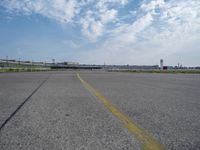 an airport runway with blue skies and some yellow lines on it and clouds in the background