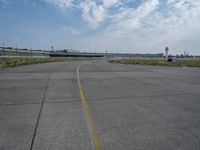 an airport runway with blue skies and some yellow lines on it and clouds in the background