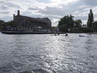 large body of water next to a building near the river with people on it and boats in the water