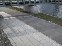 there is a person riding their bicycle on the sidewalk next to the water near a bench