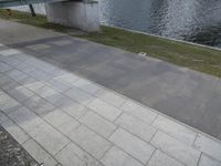 there is a person riding their bicycle on the sidewalk next to the water near a bench