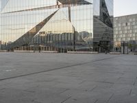 a person riding a scooter on the ground in front of a building that is reflecting other buildings