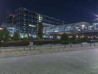 a building that is near the street with buildings in the background at night time by some lights