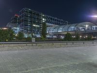 a building that is near the street with buildings in the background at night time by some lights