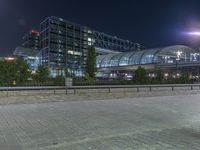 a building that is near the street with buildings in the background at night time by some lights