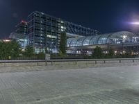 a building that is near the street with buildings in the background at night time by some lights