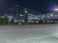 a building that is near the street with buildings in the background at night time by some lights