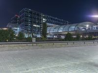 a building that is near the street with buildings in the background at night time by some lights