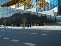 empty street near building and trees in the city on sunny day on street corner with reflections in modern glass