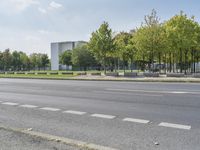 the empty street is next to trees and some buildings in the distances to it