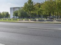 the empty street is next to trees and some buildings in the distances to it