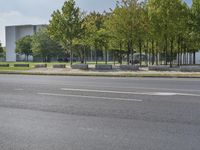 the empty street is next to trees and some buildings in the distances to it