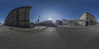 a 360 - view shows the sun through the sky above buildings on a street corner