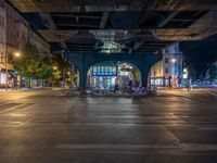 the empty street is filled with people walking and biking under an overpass at night