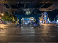 the empty street is filled with people walking and biking under an overpass at night