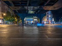 the empty street is filled with people walking and biking under an overpass at night