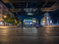 the empty street is filled with people walking and biking under an overpass at night