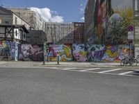 a colorful wall in an urban area with some bikes and buildings behind it - only one person is standing or sitting on the sidewalk