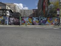 a colorful wall in an urban area with some bikes and buildings behind it - only one person is standing or sitting on the sidewalk