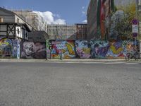 a colorful wall in an urban area with some bikes and buildings behind it - only one person is standing or sitting on the sidewalk