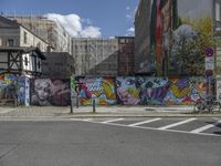 a colorful wall in an urban area with some bikes and buildings behind it - only one person is standing or sitting on the sidewalk