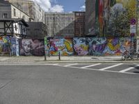 a colorful wall in an urban area with some bikes and buildings behind it - only one person is standing or sitting on the sidewalk