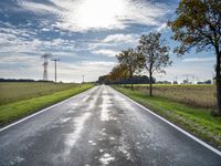 an empty road runs through a grassy plain area and with power lines in the background