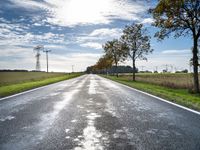 an empty road runs through a grassy plain area and with power lines in the background