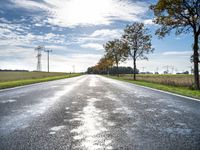 an empty road runs through a grassy plain area and with power lines in the background